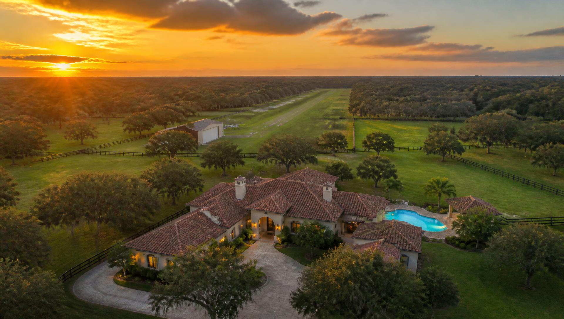 Aerial view of the 4460 Runway Ln estate at sunset with grass runway, pasture and pool